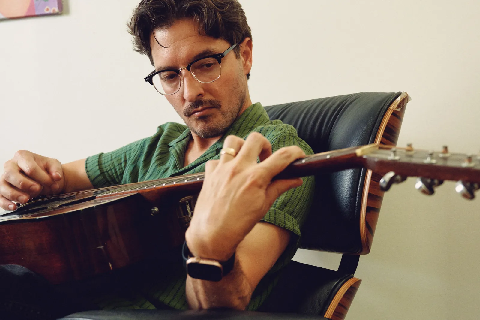 Graham Hill playing acoustic guitar in a leather chair