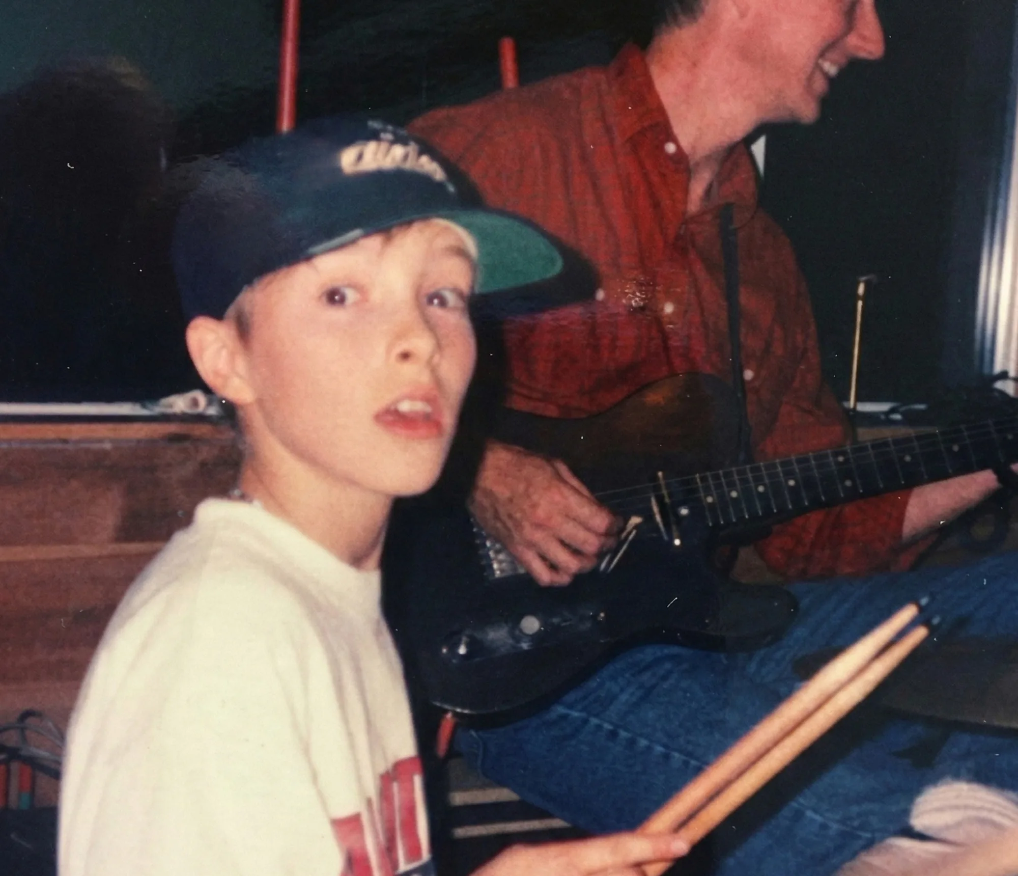 Young Graham Hill in a baseball cap, drumsticks in hand, with his father Steve Hill playing guitar behind him